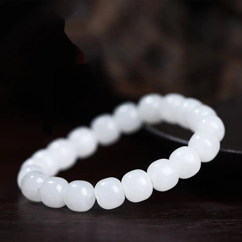 White Hetian jade barrel bead bracelet for men and women on a wooden surface.
