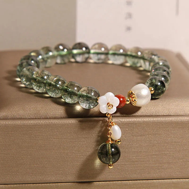 Green phantom quartz crystal bracelet with shell flower charm on a woman's wrist