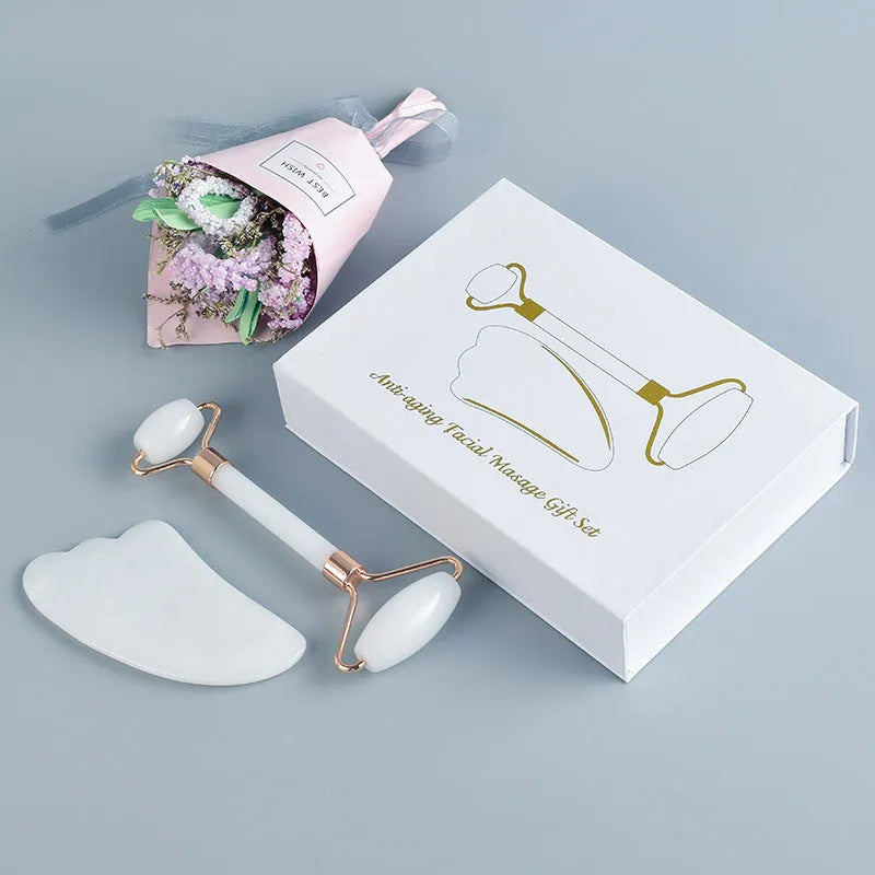 White jade facial roller with double heads and a matching gua sha scraping board on a plain surface.