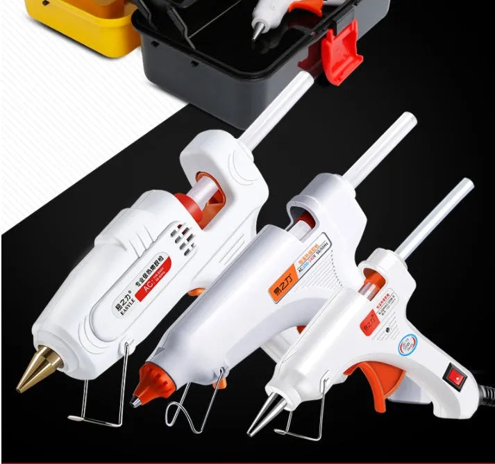 White electric hot glue gun with metal stand and glue sticks on a workbench.