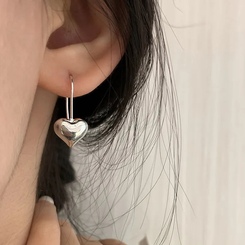 Silver coloured heart-shaped earrings with three-dimensional design and ear hooks
