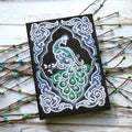 Black A5 diamond painting notebook open to a peacock design with shaped and bright sparkling drills