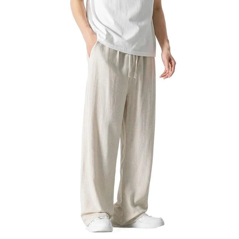 Men's beige loose straight-leg linen trousers with a drawstring waist, shown in a casual summer setting.