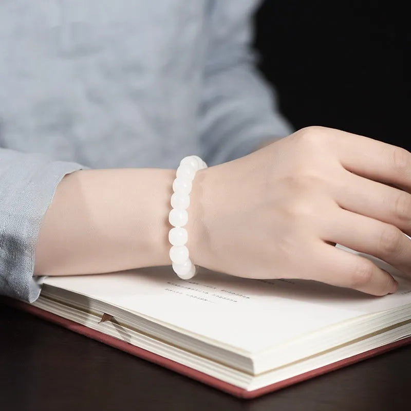 White Hetian jade barrel bead bracelet for men and women on a wooden surface.
