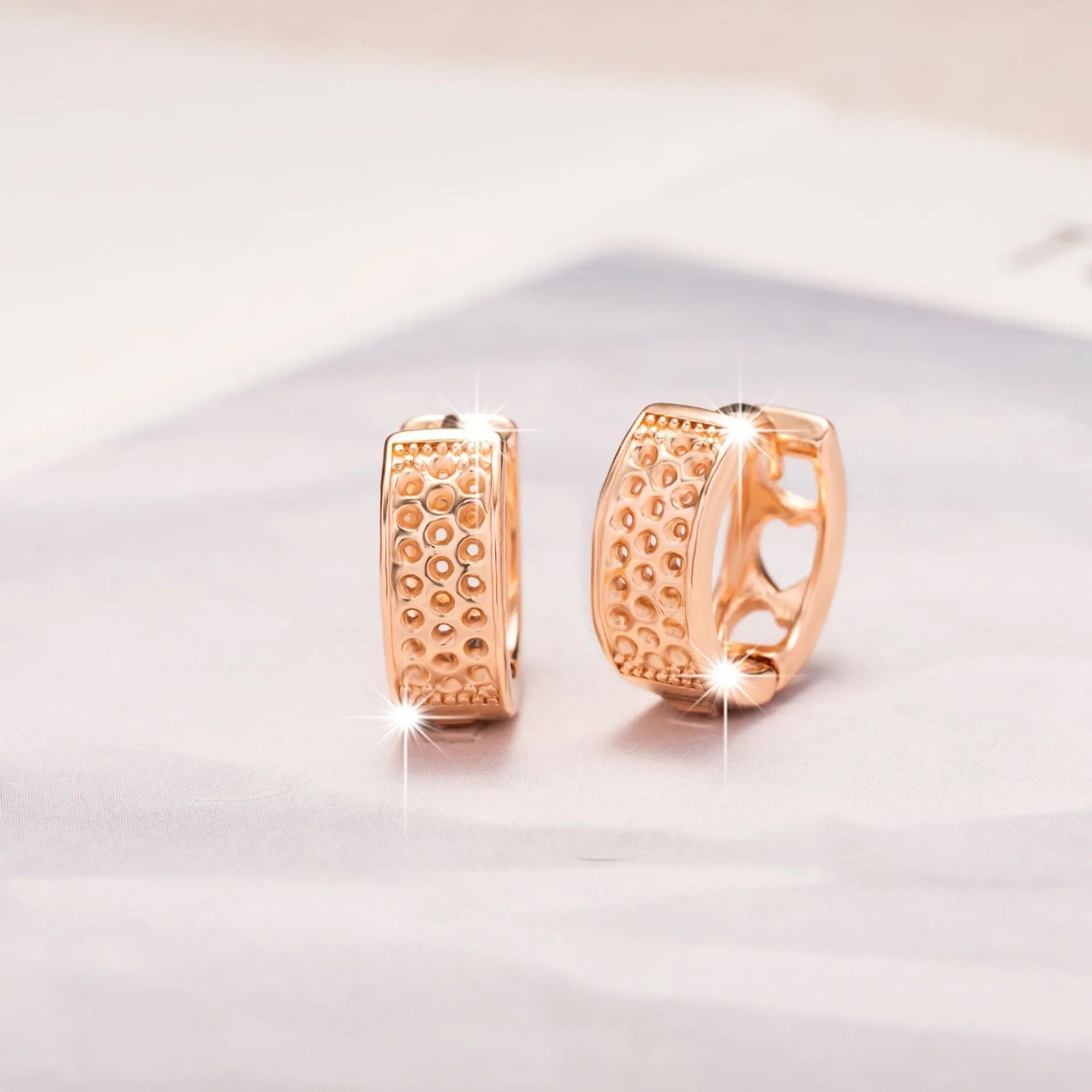 Rose gold circular earrings with three hollowed-out heart shapes.