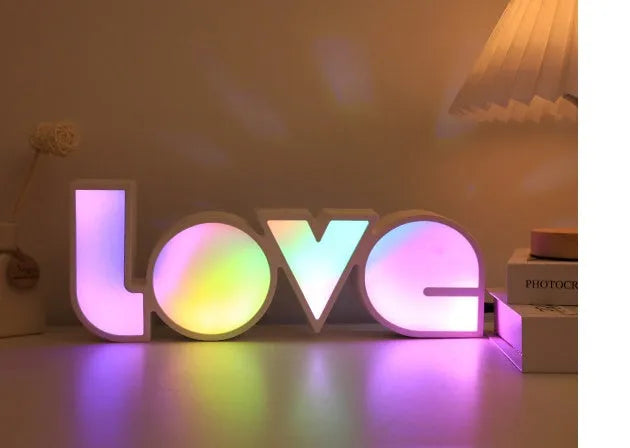 Rainbow style plastic LED decorative light spelling LOVE, shown on a table.