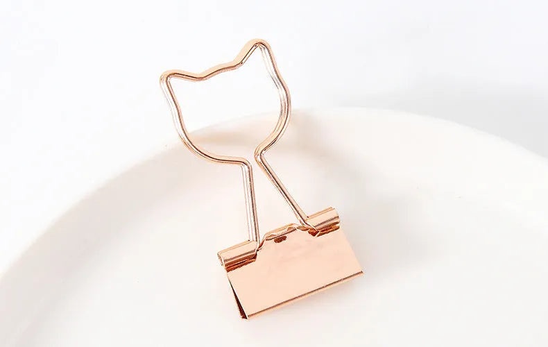 Gold metal clip with a decorative bow charm, shown holding papers.