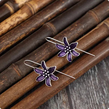 A pair of purple flower-shaped alloy stud earrings with a simple post back, shown against a plain background.