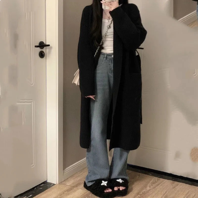 Loose large dark grey knitted cardigan with a 3D pattern, worn open over a top.