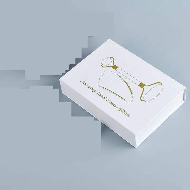 White jade facial roller with double heads and a matching gua sha scraping board on a plain surface.