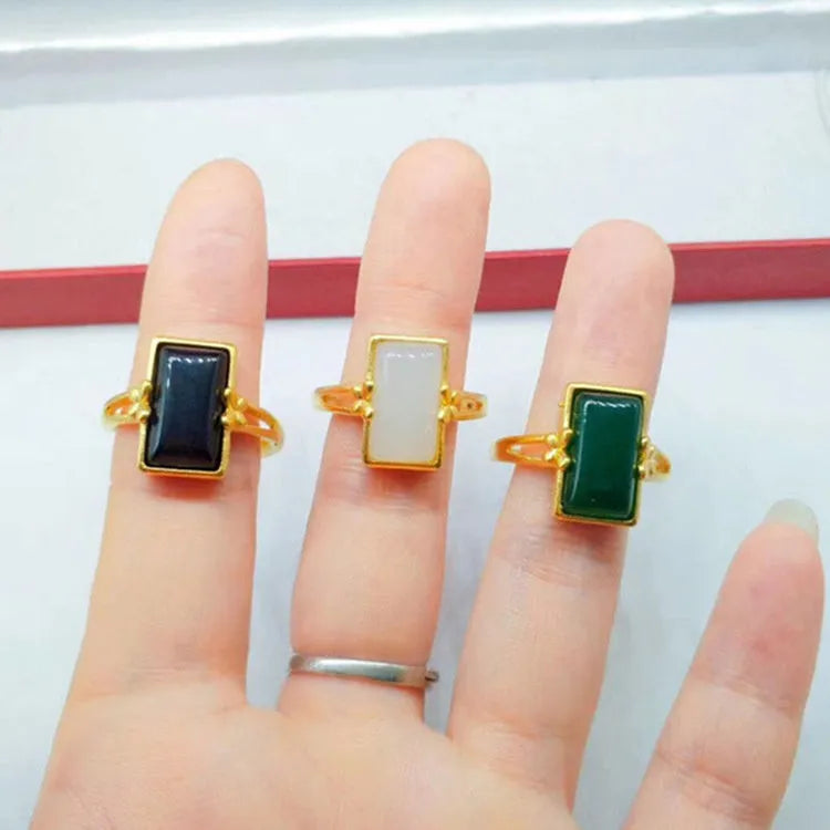 Adjustable gold-plated brass ring with a black artificial gemstone on a neutral background.
