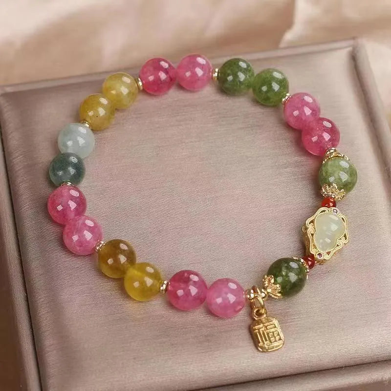 Women's bracelet with colourful tourmaline gourd blessing charm and floral clasp on a mixed material chain.