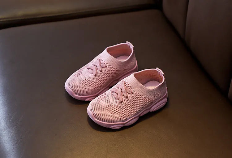 Children's white fabric lazy slip-on shoe with a non-slip rubber sole on a wooden floor.