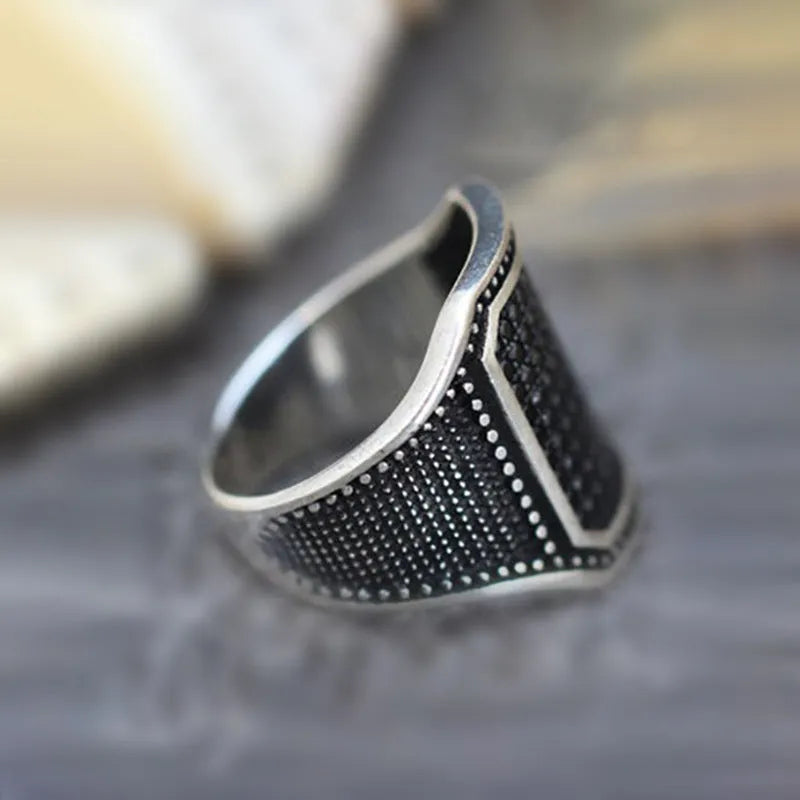 A black alloy ring with copper inlay and a centred zircon stone, shown on a finger.