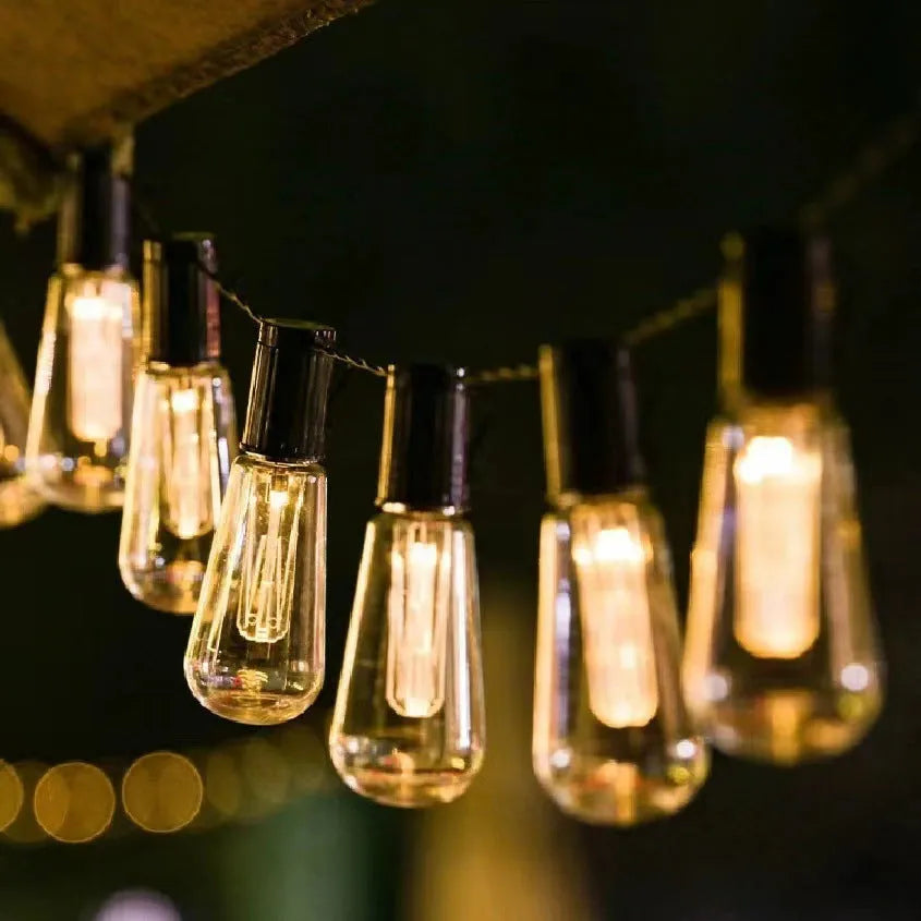 Retro infusion bottle shaped solar outdoor string lights draped in a garden setting.