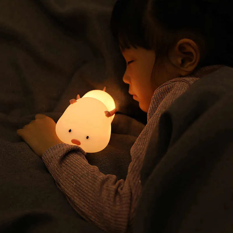 Blue silicone pig-shaped rechargeable LED night light with touch control on a wooden surface.