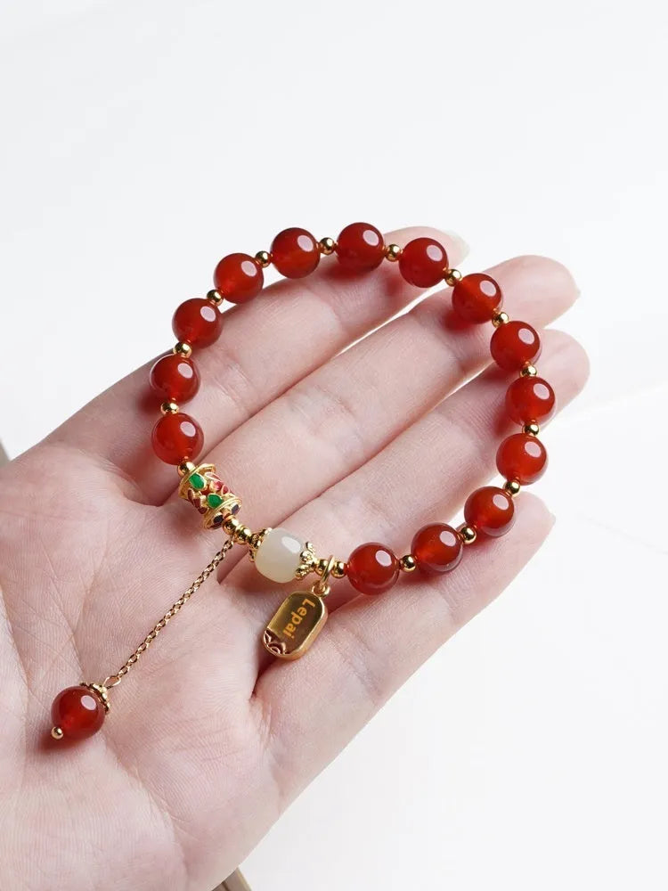 A women's bracelet with red agate beads and gold-plated metal elements on a wrist.