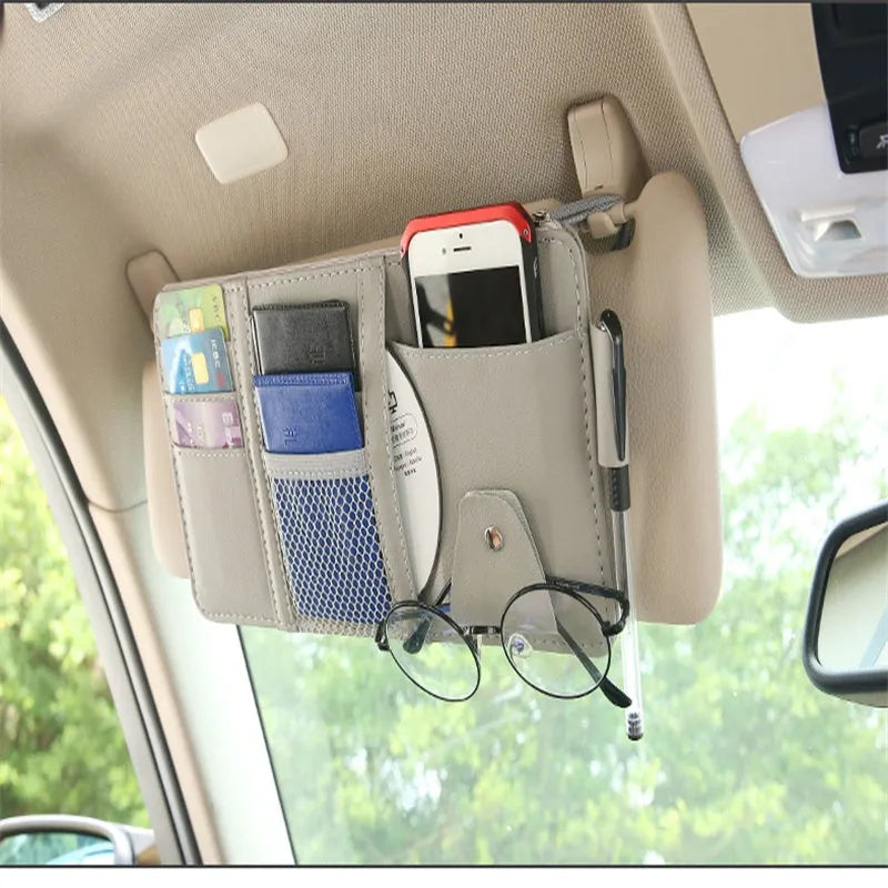 Beige car sun visor storage bag with seven open pockets, zip pocket, sunglasses clip, and pen holder on vehicle visor