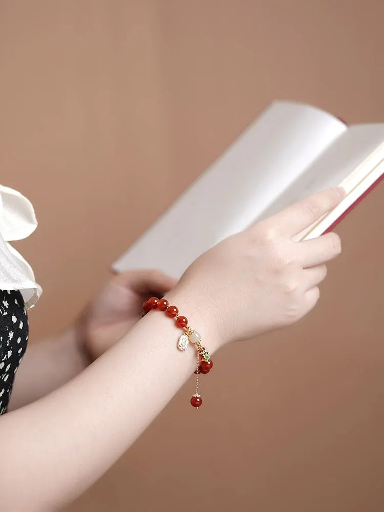 A women's bracelet with red agate beads and gold-plated metal elements on a wrist.