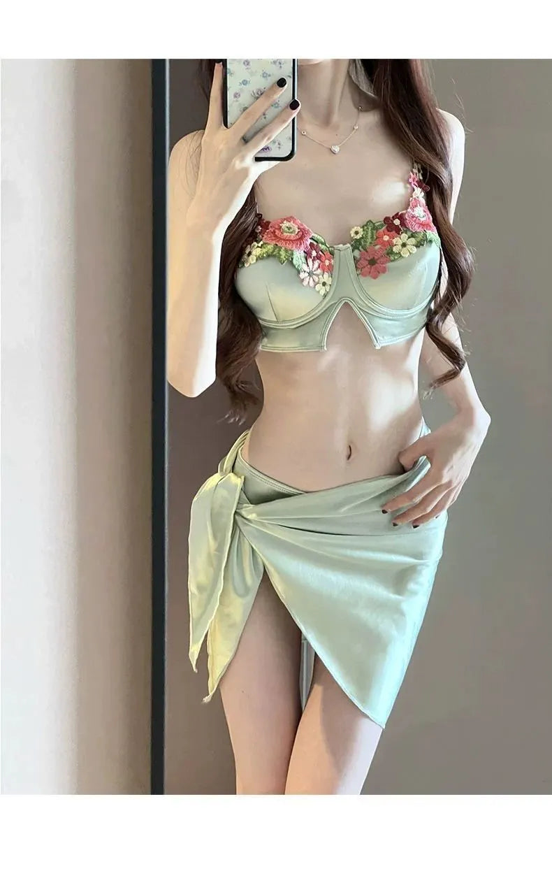 Green women's three-piece bikini set with triangle top, briefs, and skirt on white background