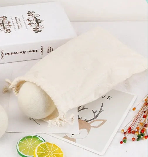 A white wool felt drying ball for laundry next to a plain cotton storage bag on a blue background.