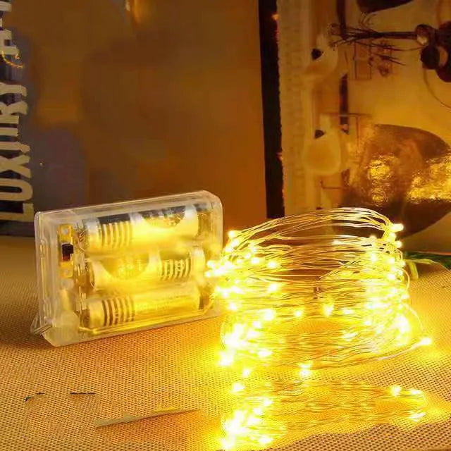 Copper wire LED string light with 120 bulbs, coiled to show its 12-metre length and battery box with USB cable.