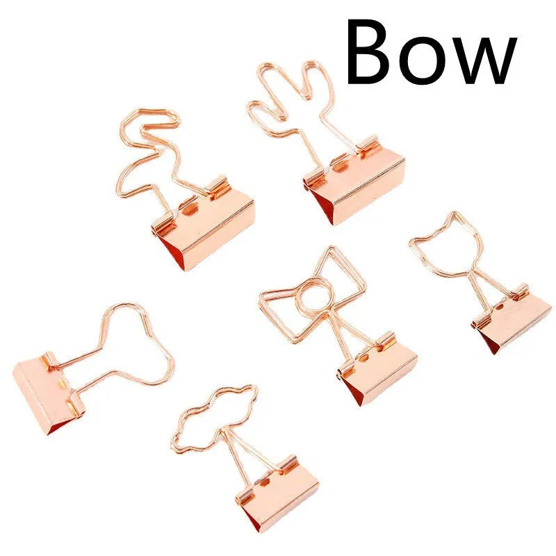 Gold metal clip with a decorative bow charm, shown holding papers.