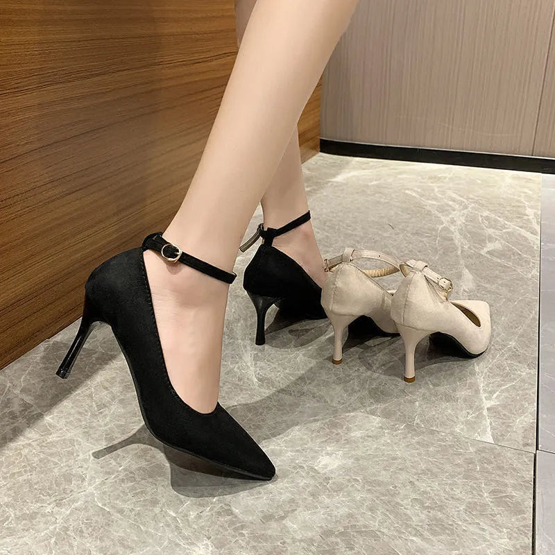 Women's black stiletto heel pumps with skull pattern and buckle detail on wooden floor