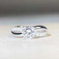 Geometric silver ring with a 1 karat moissanite stone in a four-claw setting and twisted arm band.