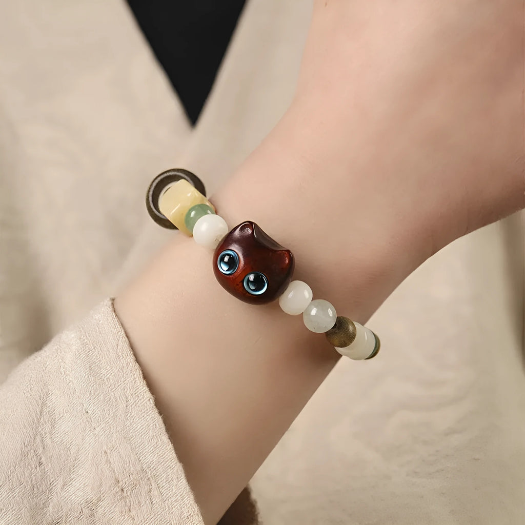 Hand-woven cat paw bracelet with a jade, bodhi seed, and ebony multi-treasure cube charm.