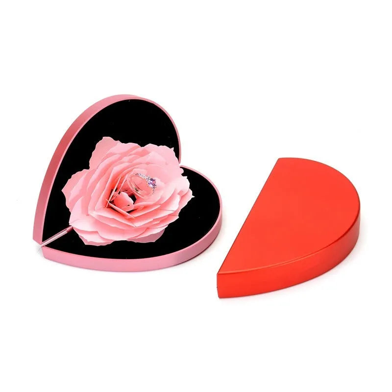 Red plastic heart-shaped rotating ring box with rose decoration inside white storage case