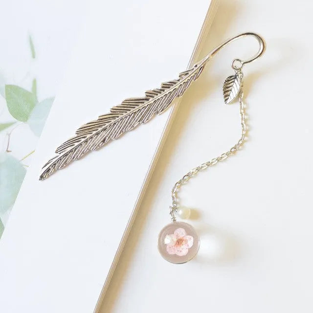 Close-up of a dried flower specimen sealed within a slim, silver-toned alloy metal bookmark.