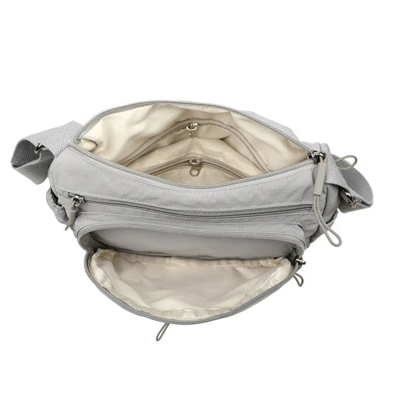 Grey water-repellent nylon crossbody bag showing front three-dimensional pocket and adjustable shoulder strap.