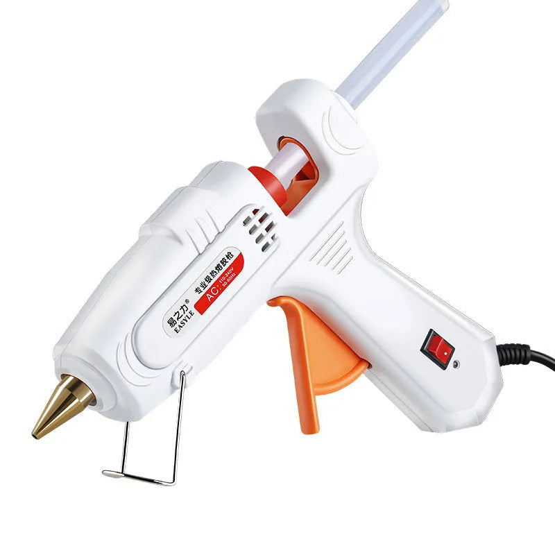 White electric hot glue gun with metal stand and glue sticks on a workbench.