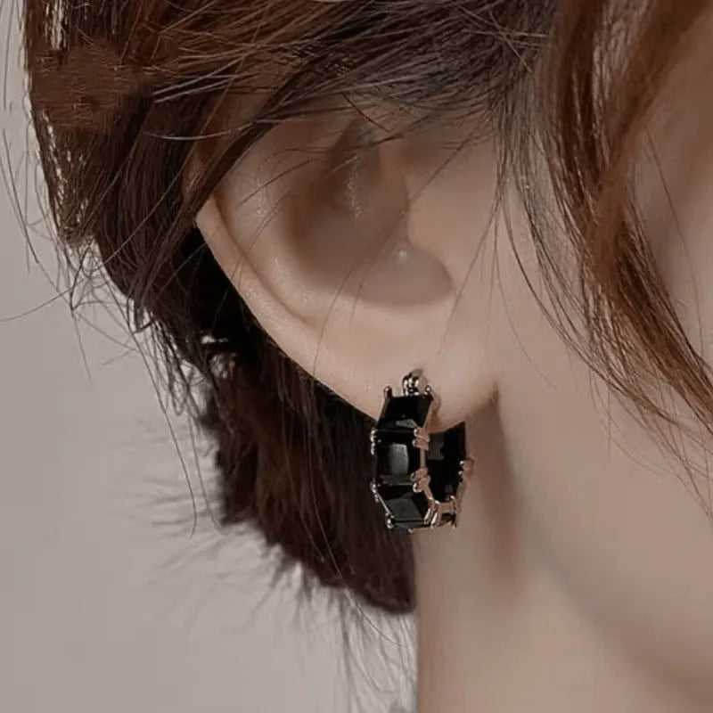 Women's geometric U-shaped gold earrings with round black zircon crystals on white background