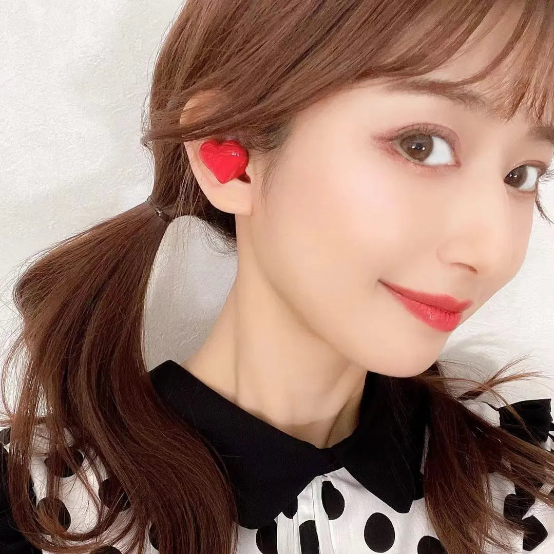 Heart-shaped wireless Bluetooth headphones in red or pink with in-ear design and charging cable
