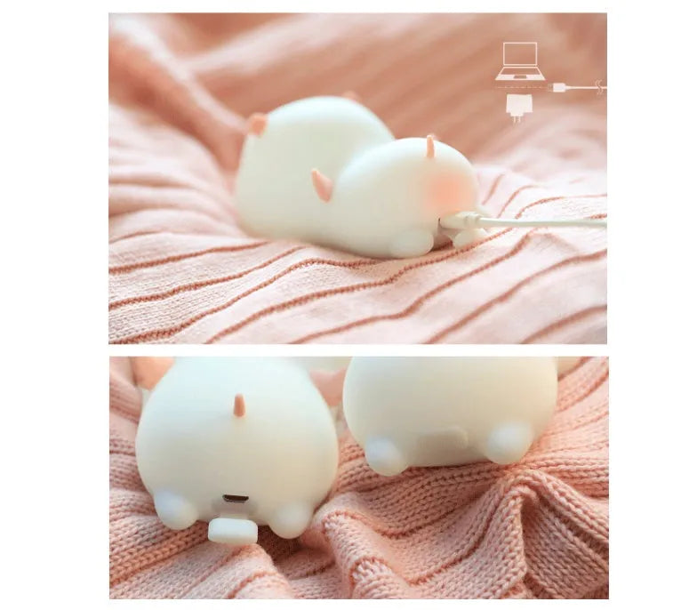 Blue silicone pig-shaped rechargeable LED night light with touch control on a wooden surface.