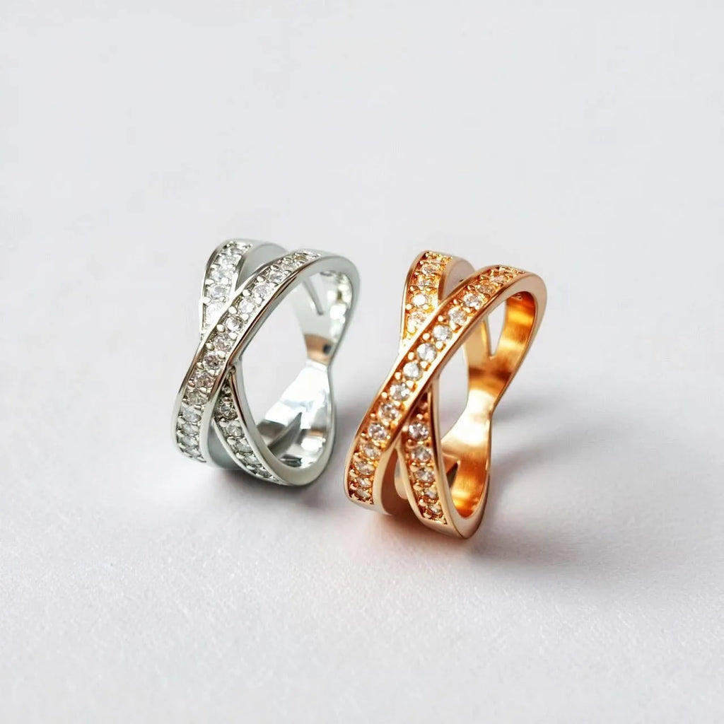 Silver or rose gold metal cross ring with micro-inlaid zircon accents on a plain background.