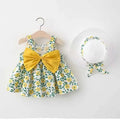 Baby girl wearing a yellow cotton flower print suspender dress with matching hat on a summer background