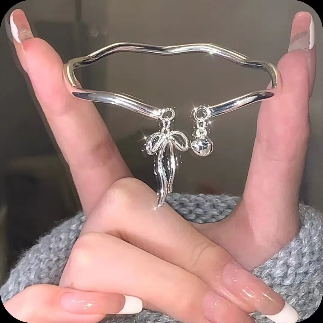 Silver adjustable girlfriends bracelet with bow and bell charm on a wrist.