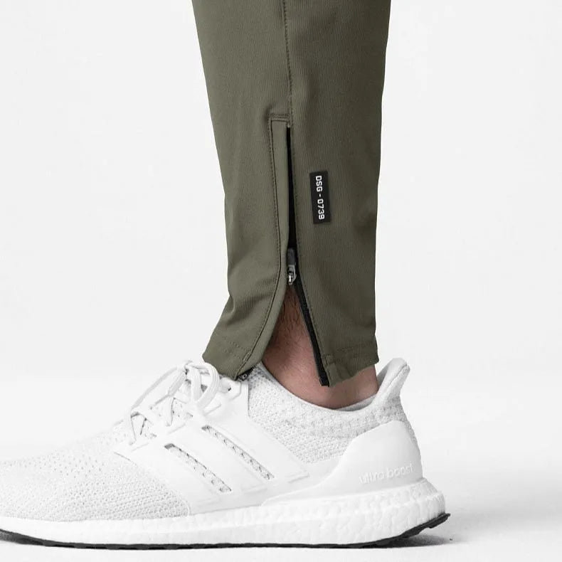Man wearing loose grey running trousers with tied ankles, made from quick-dry polyester fabric.