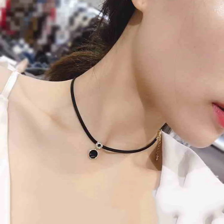 Women's short black clavicle necklace with round gold alloy pendant and leather rope chain on display