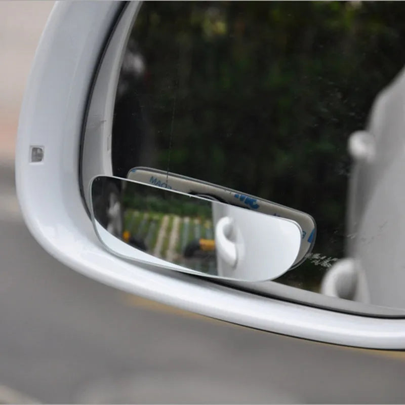 Glass adjustable blind spot mirror with angle bracket shown next to a vehicle rearview mirror.