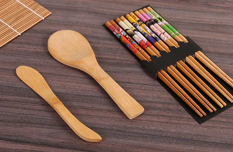 White sushi tool set with bamboo rolling mat, rice paddle, and sushi mold on a surface.