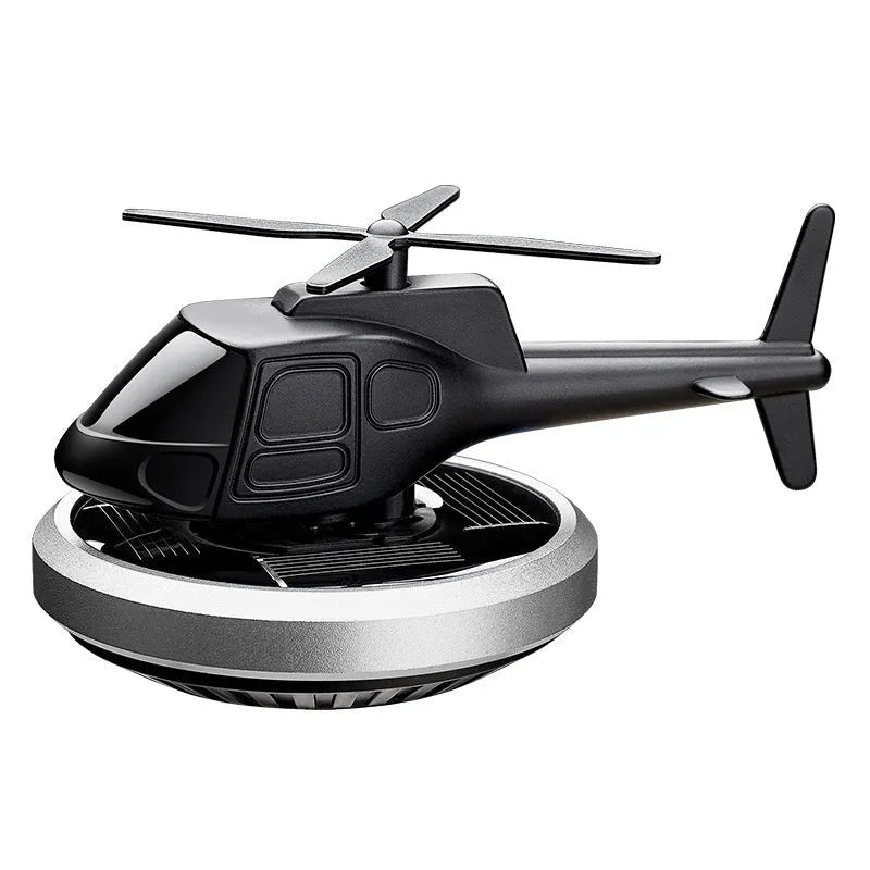 Silver solar-powered metal helicopter car air freshener ornament with spinning blades on a dashboard.