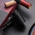 Automatic electric wine opener with black ABS shell and foil cutter set on a table alongside a wine bottle