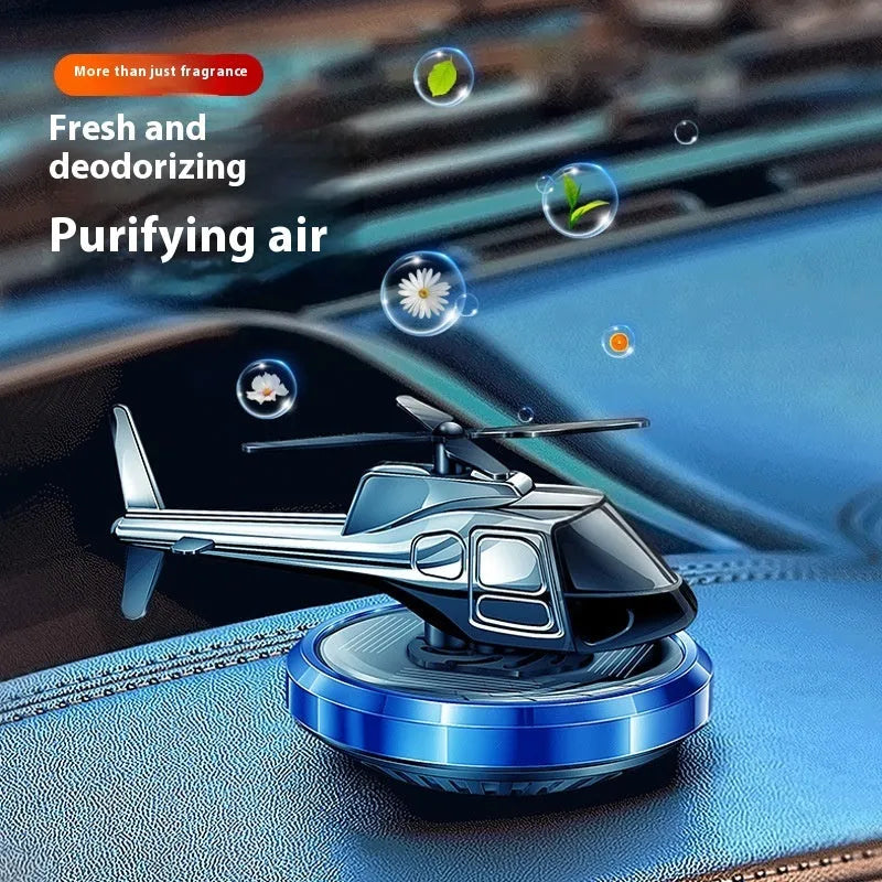 Silver solar-powered metal helicopter car air freshener ornament with spinning blades on a dashboard.
