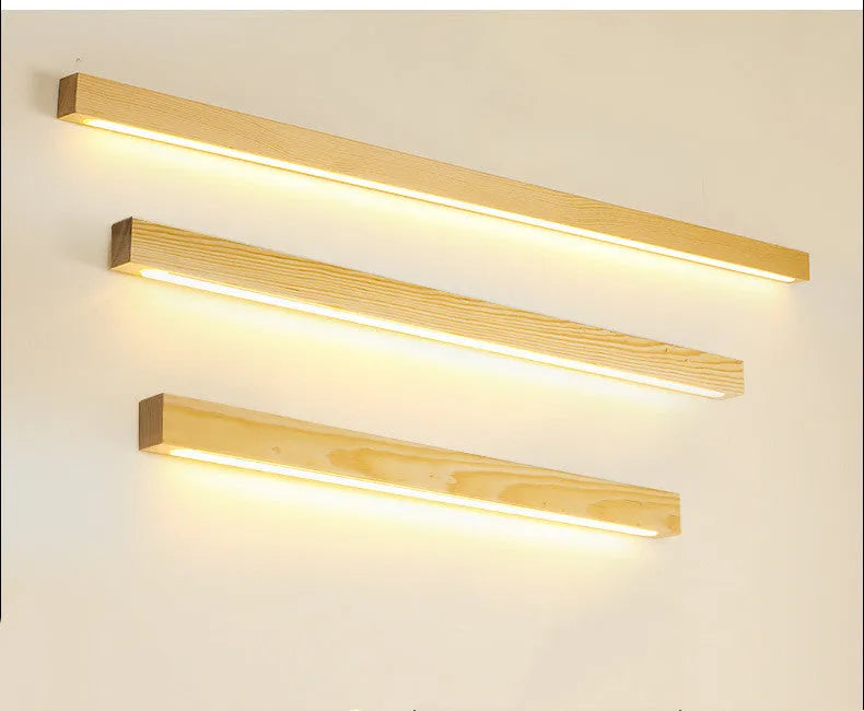 Slim, long walnut-coloured wooden strip wall lamp mounted on a plain wall.