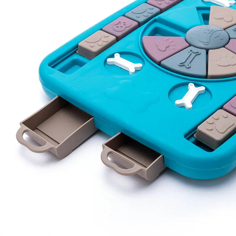 Blue plastic interactive dog puzzle feeder with sliding panel and four corner handles on a non-slip base
