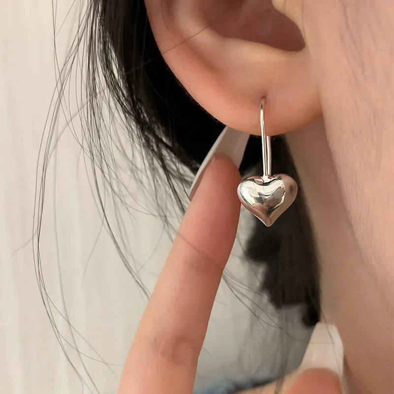 Silver coloured heart-shaped earrings with three-dimensional design and ear hooks